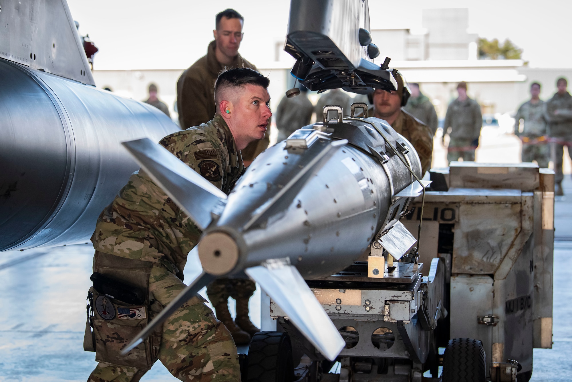 Military members in uniform attach a missile to an F-16.
