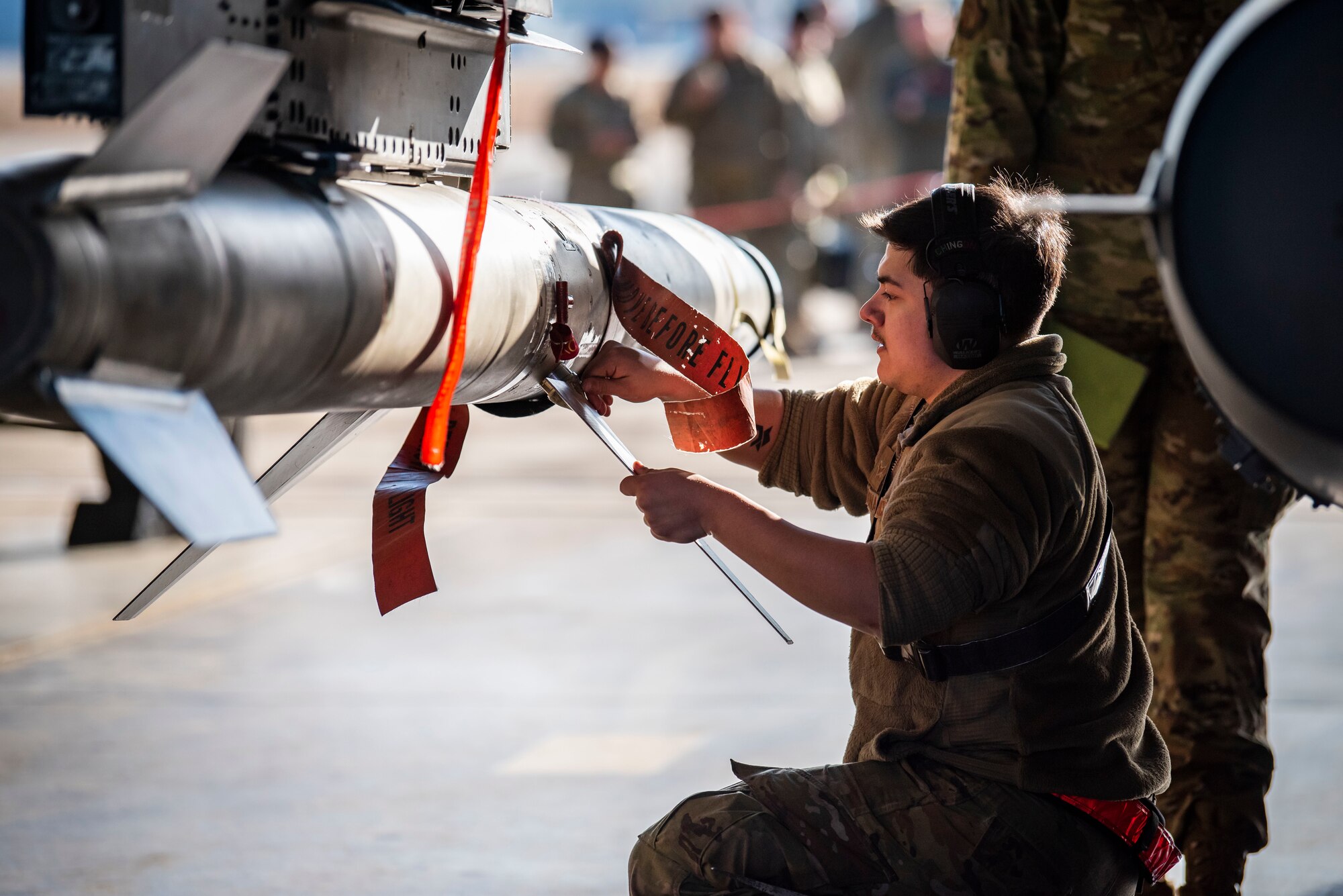 Man in military uniform attaches fins to a missile.