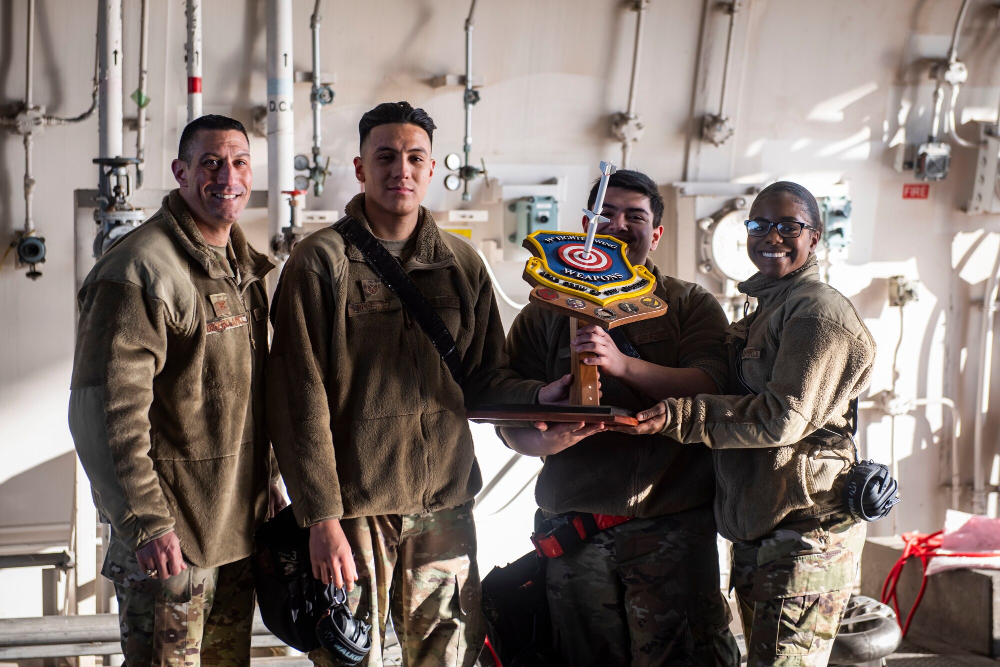 Men and women in military uniform hold a trophy.