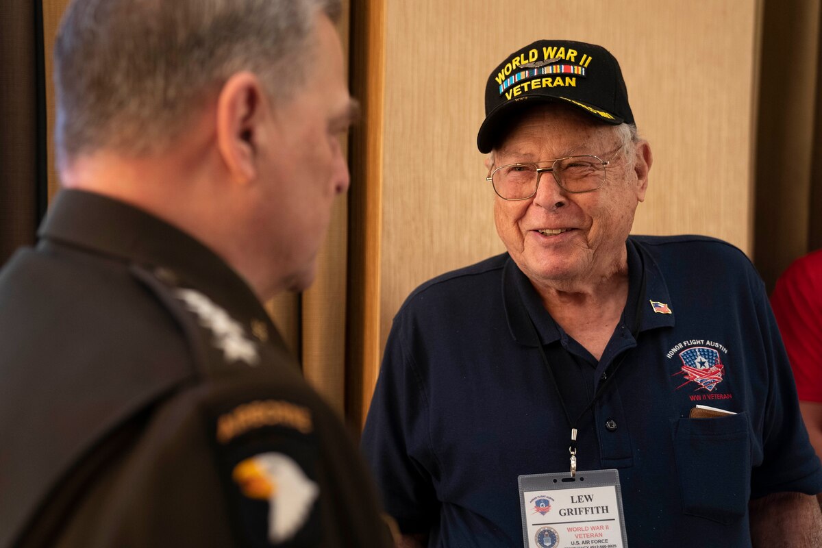 A man wearing a World War II veteran’s baseball-style cap speaks with a man in uniform.