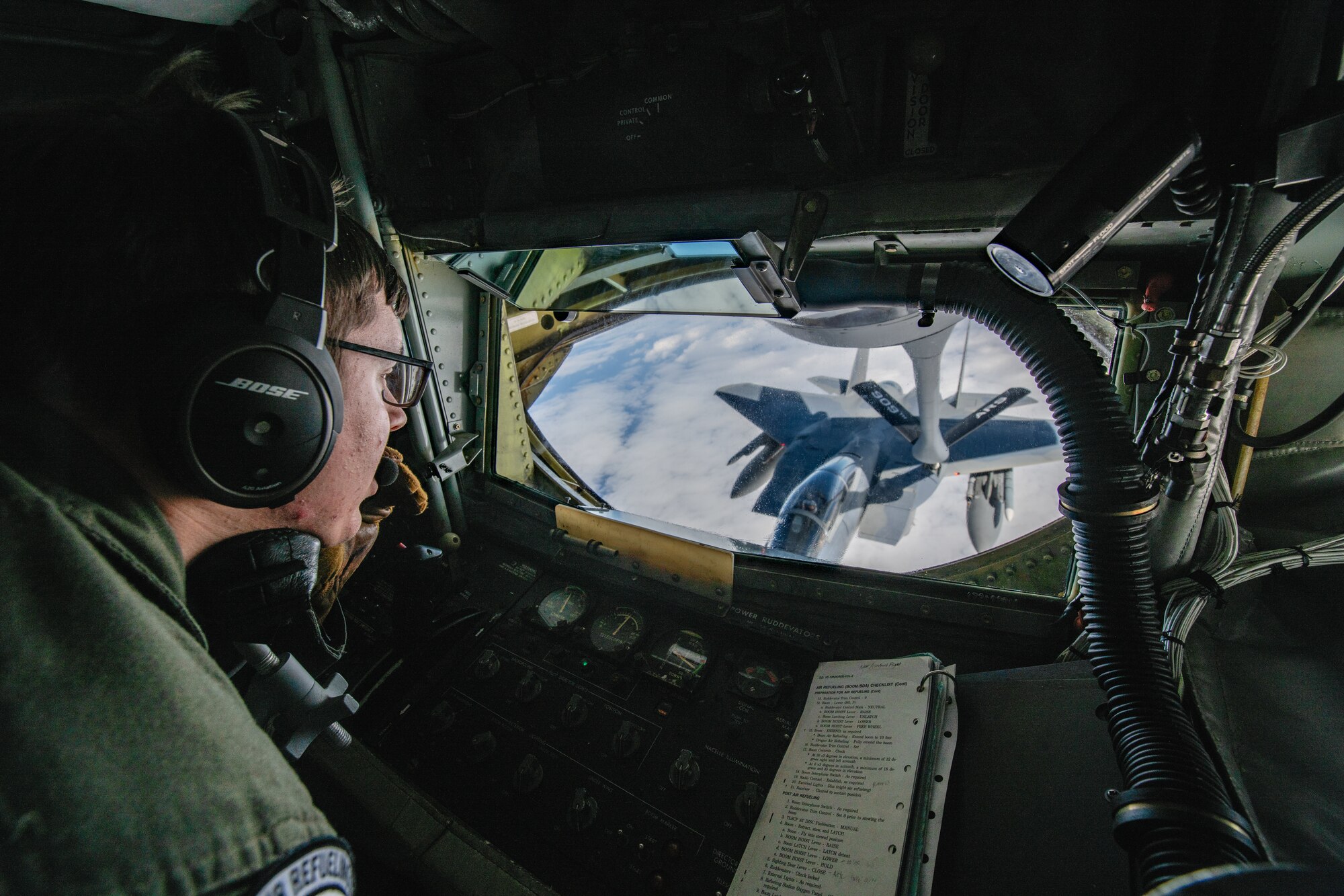 A boom operator looks out the back of a KC-135 Stratotanker at a fighter jet he's refueling