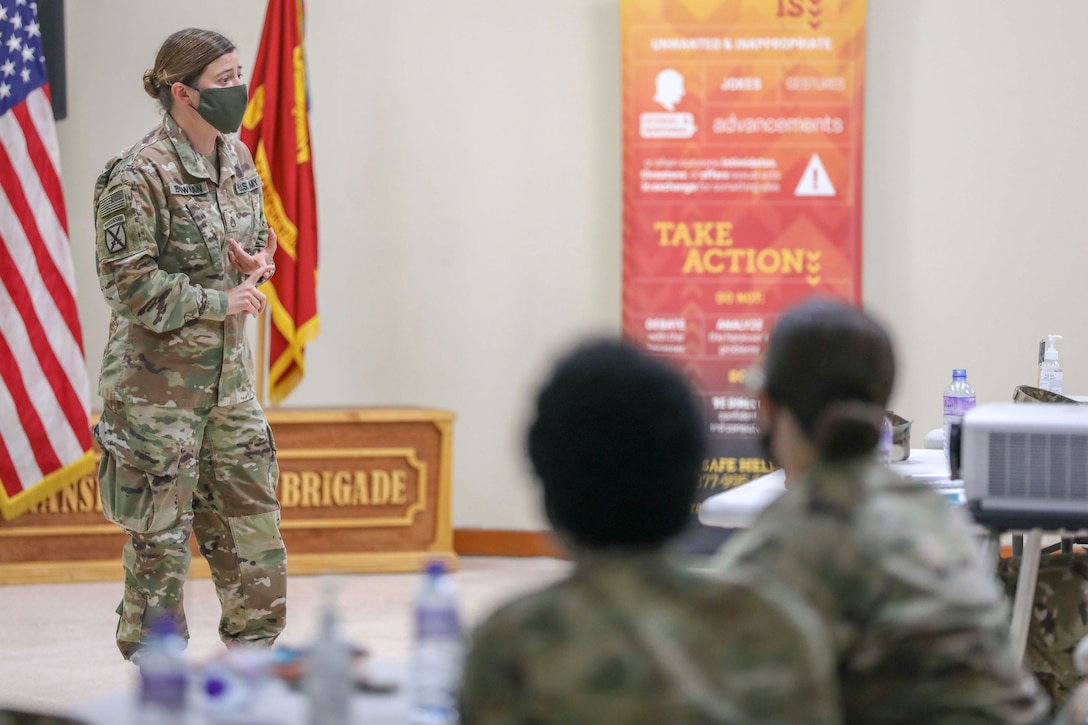 A soldier stands at the front of a room to give a lecture to seated students.