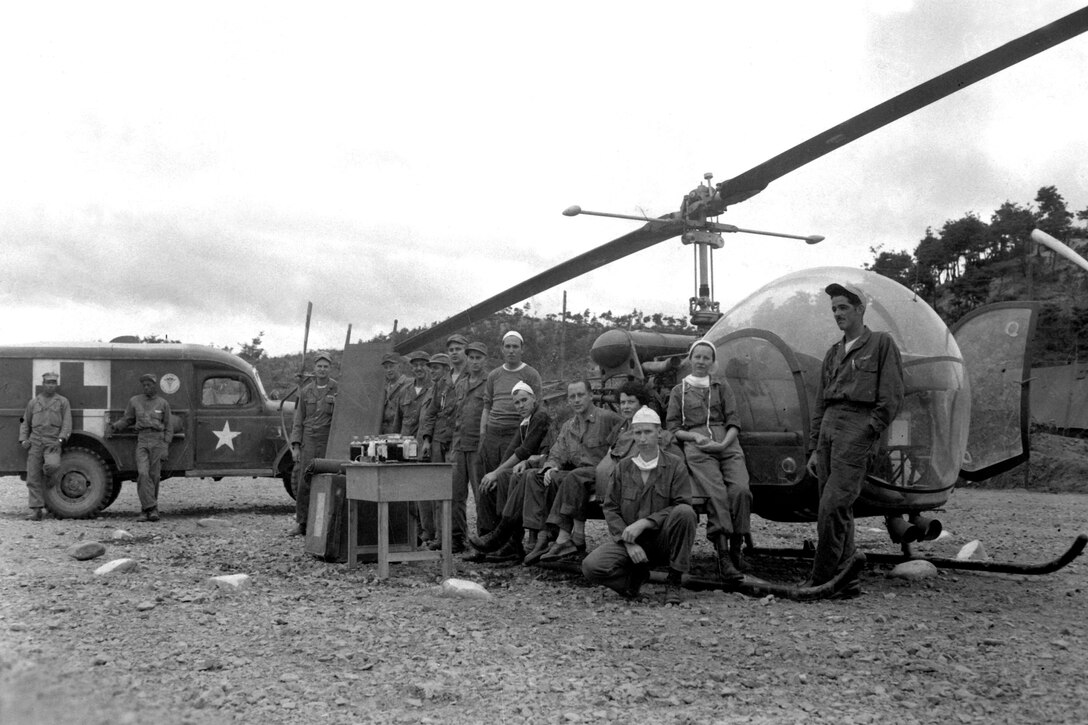 People pose for a photo in front of a helicopter and ambulance.