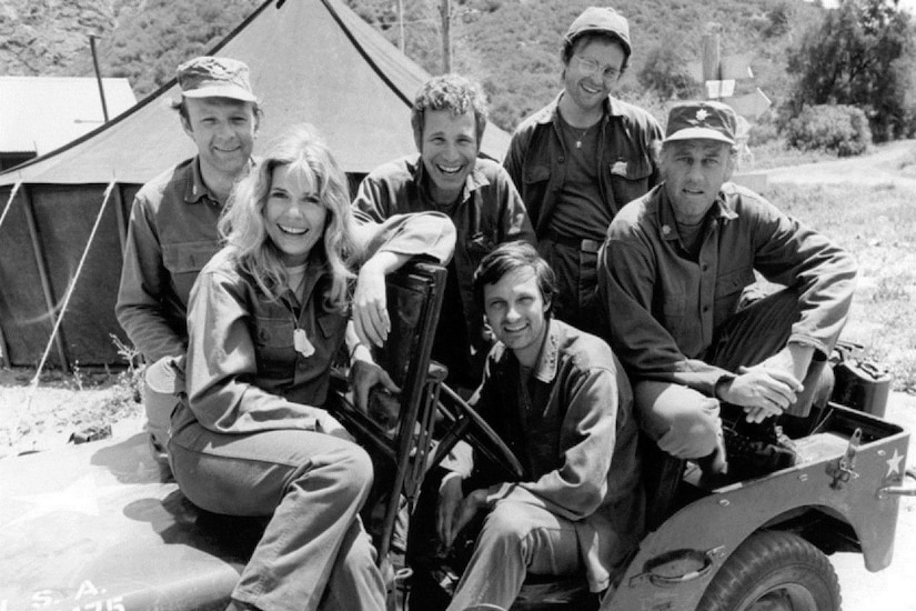 Five men and one woman pose for a photo in a jeep.