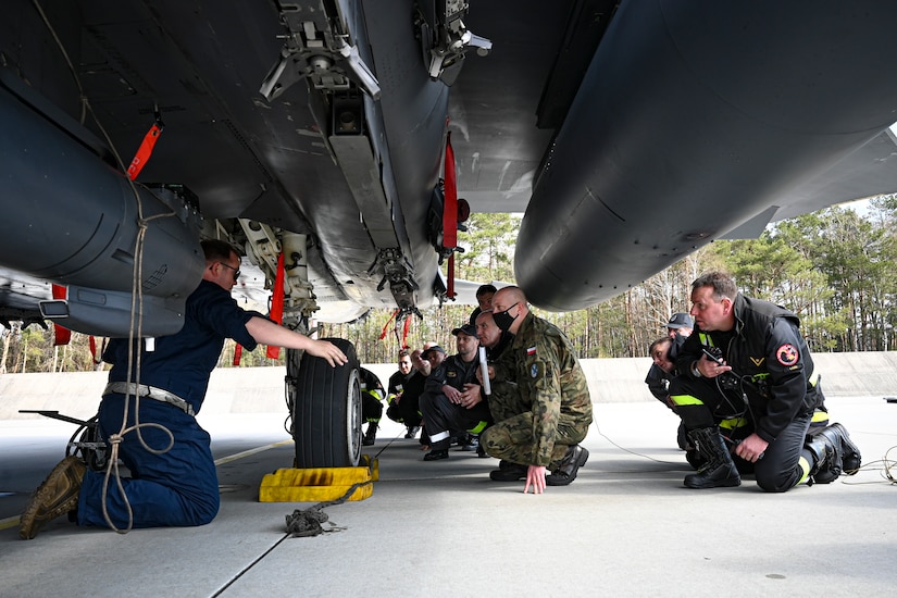 Air Force and Polish firefighters examine the underside of an F-15.