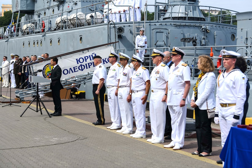 Ukrainian president and senior naval officers in a line in front of a ship.