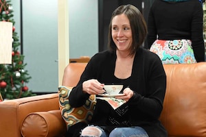 Woman smiles while drinking tea on couch.