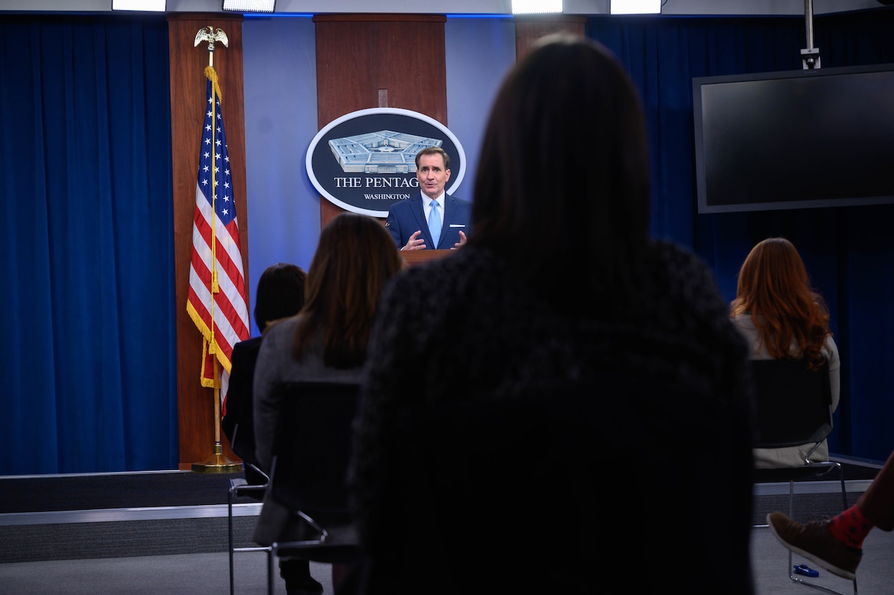 A man speaks from a lectern during a briefing to a socially distanced audience.