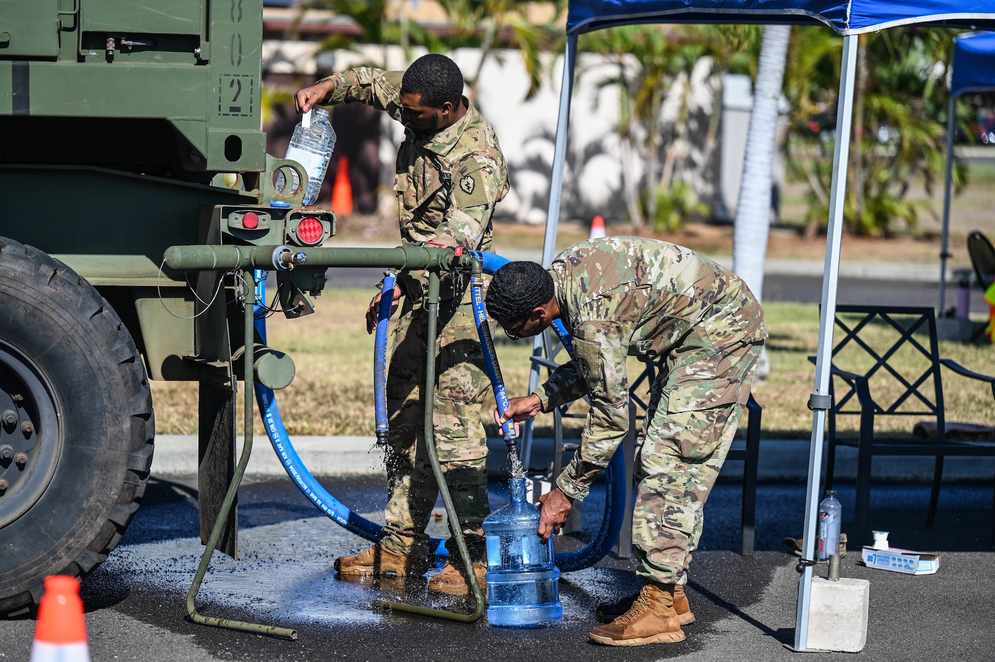 Army Spc. Cartia Carter and Pvt. Darien Forsythe, 524th Division Sustainment Support Battalion petroleum supply specialists, refill containers with water from a 2K Potable Water Module at the Hickam Makai Recreation Center at Joint Base Pearl Harbor-Hickam, Hawaii, Dec. 2, 2021. The Army provided a 24-hour service, refilling reusable water containers for affected personnel. (U.S. Air Force photo by Staff Sgt. Alan Ricker)