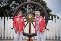 PEARL HARBOR, Hawaii (Dec. 7, 2021) - "Rosie" Marian Wynn (left) and "Rosie" Mae Krier stand before the Helm of the USS Oklahoma (BB-37) on the 80th anniversary of the attack on Pearl Harbor when 429 Sailors and Marines on board lost their lives. Wynn was a shipyard worker while Krier built B-17 and B-29 aircraft bombers during the war. (U.S. Navy Photo by MC1 Jeffrey Hanshaw/Released).