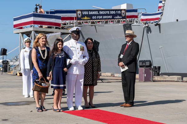 PEARL HARBOR, Hawaii (Dec. 8, 2021) Command Master Chief Simeon Yeboah escorts Matrons of Honor Jessica Carroll Inouye, left, Jennifer Goto Sabas, right, and 11-year-old Maid of Honor Maggie Inouye, during the commissioning ceremony of USS Daniel Inouye (DDG 118). Homeported at Joint Base Pearl Harbor-Hickam, DDG 118 is the first U.S. Navy warship to honor the Honorable Daniel K. Inouye, a U.S. senator from Hawaii who served from 1962 until his death in 2012. During World War II, Inouye served in the U.S. Army’s 442nd Regimental Combat Team, one of the most decorated military units in U.S. history. For his combat heroism, which cost him his right arm, Inouye was awarded the Medal of Honor. (U.S. Navy photo by Mass Communication Specialist 1st Class Kelby Sanders)