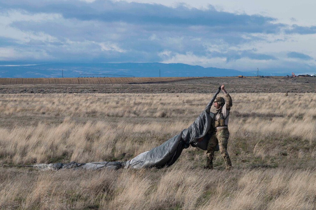 An airman pulls in a parachute in a field.