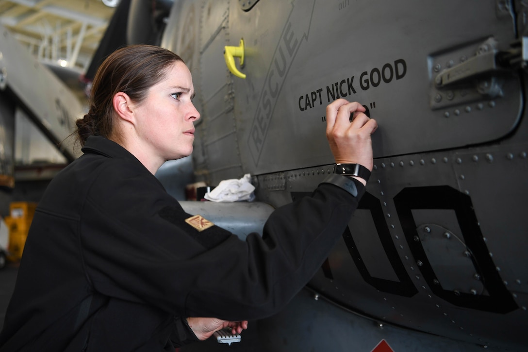 A sailor applies markings on an aircraft.