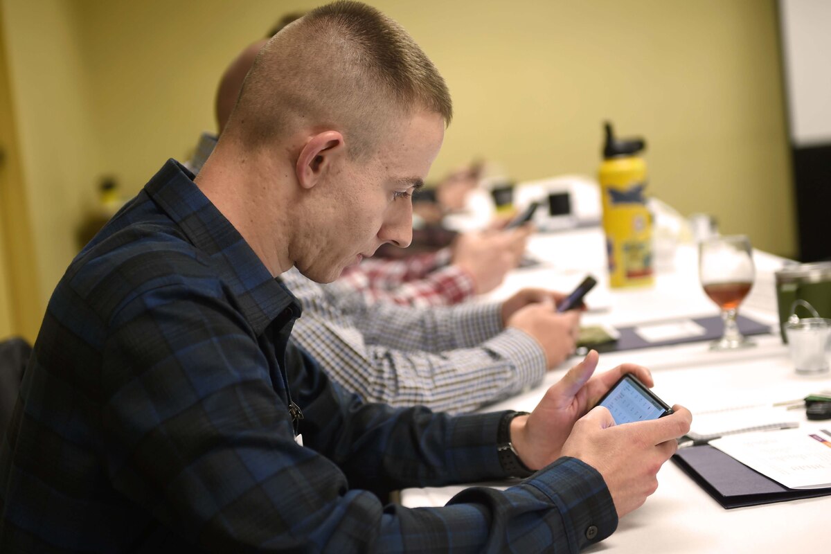 Men sitting in a row at a table use their mobile phones to take a survey.