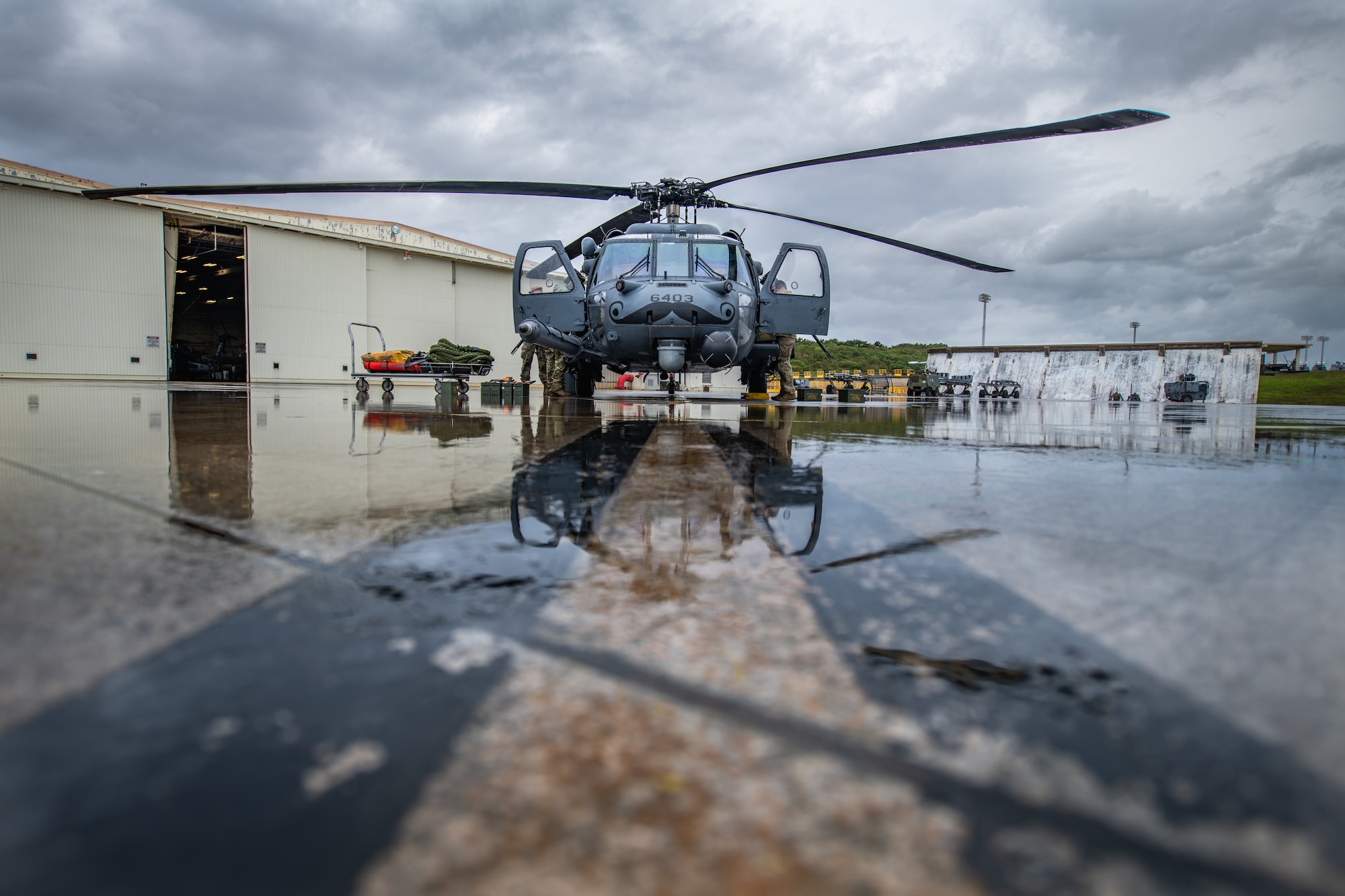 A helicopter sits outside a hangar on wet pavement
