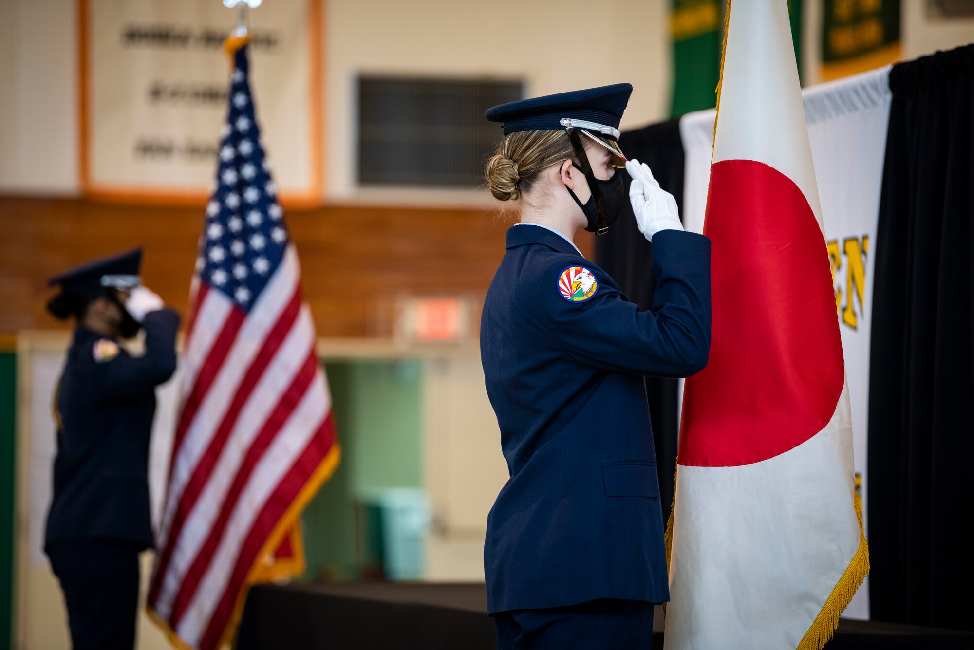 Two ladies in Air Force Blues salute the Japanese and United States flags, respectively.
