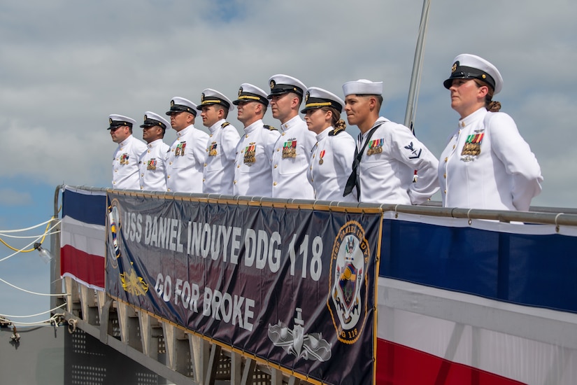 Sailors stand in line on the rail of a ship.