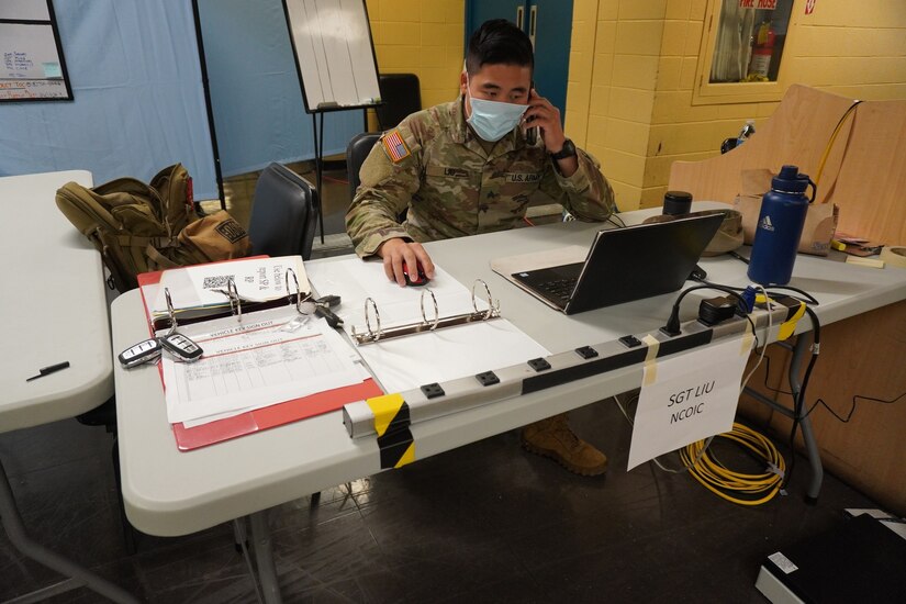 A soldier sits at a desk and talks on the phone.