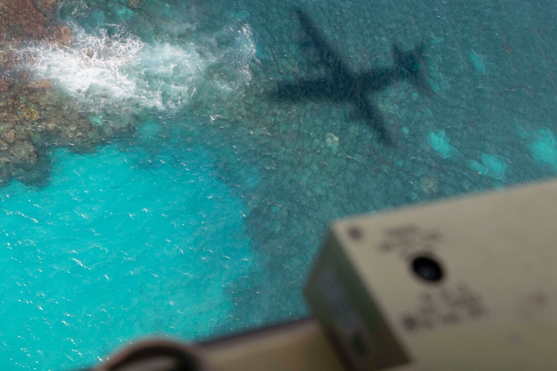 The shadow of an aircraft is seen as it flies over blue water.