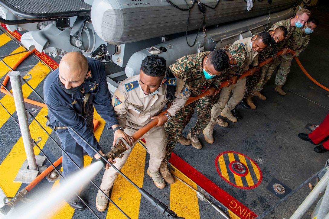 A group of men in uniform hold a hose that is spraying water.