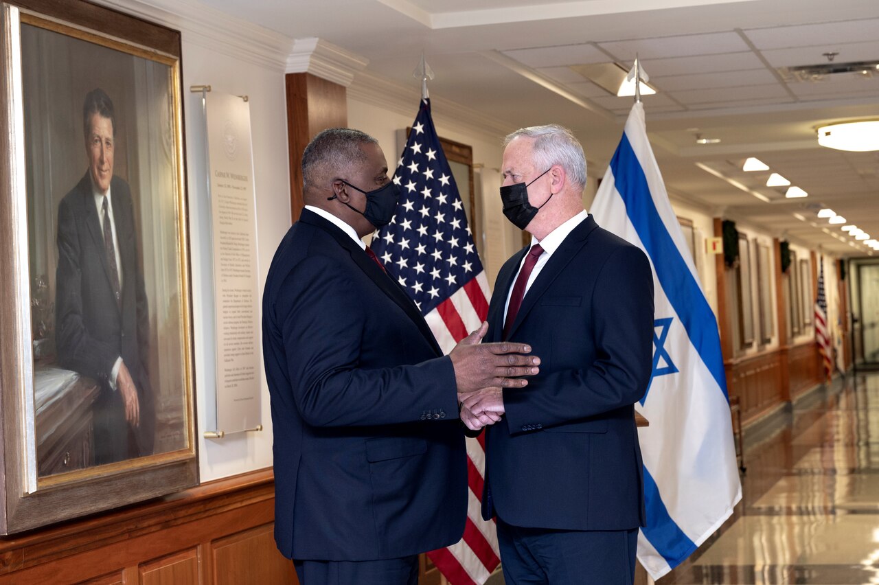 Two men in suits stand before the flags of the United States and Israel.