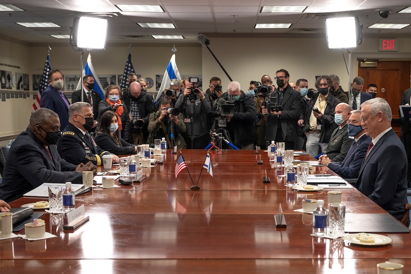 Multiple individuals, some in uniform, sit across from each other at a table.