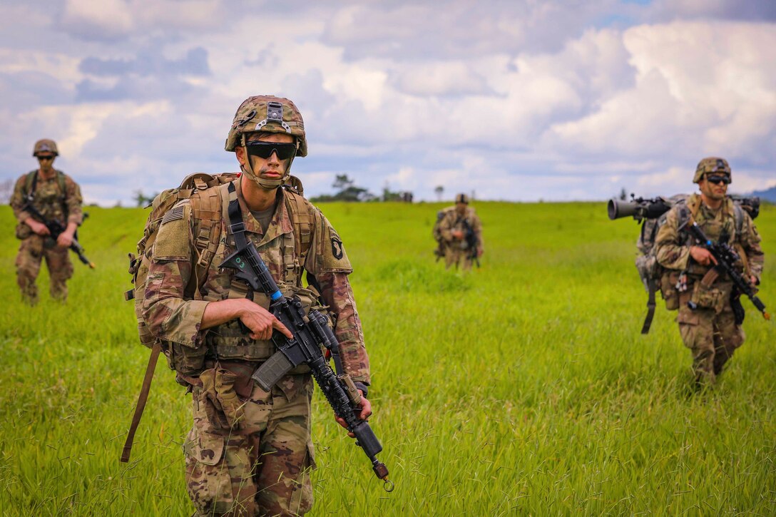 A group of soldiers walk through a grassy field.