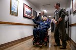 A man in a wheelchair points at a picture on the wall as others stand near him.