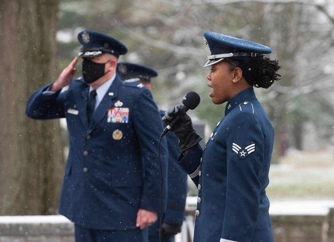 Senior Airman MeLan Smartt sings the national anthem as Col. Patrick Miller, 88th Air Base Wing and installation commander, salutes at the start of the annual ceremony, held at the Wright Brothers Memorial on Wright-Patterson Air Force Base, Ohio, Dec. 17, 2020, marking the 117th anniversary of the first powered flight. The memorial overlooks Huffman Prairie where the Wright Brothers taught themselves and others how to fly. (U.S. Air Force photo by R.J. Oriez)