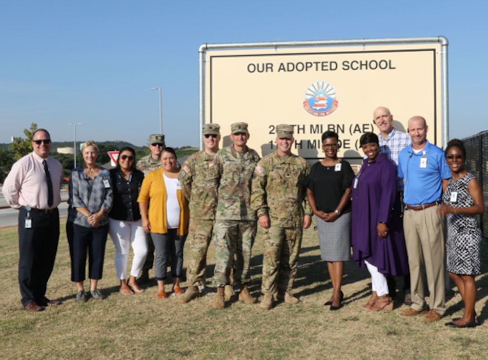 Group of school officials and military members in front of a sign labelled "Our Adopted School."