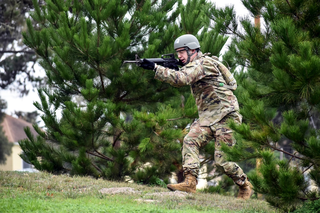 A soldier pointing a weapon walks forward on a field.
