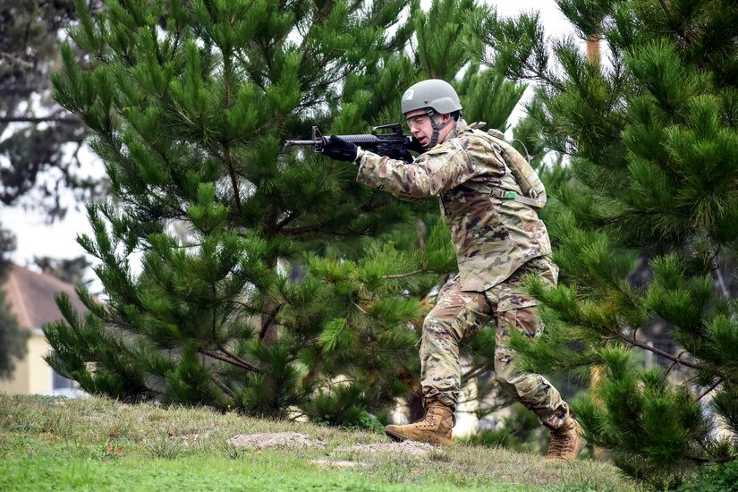 A soldier pointing a weapon walks forward on a field.