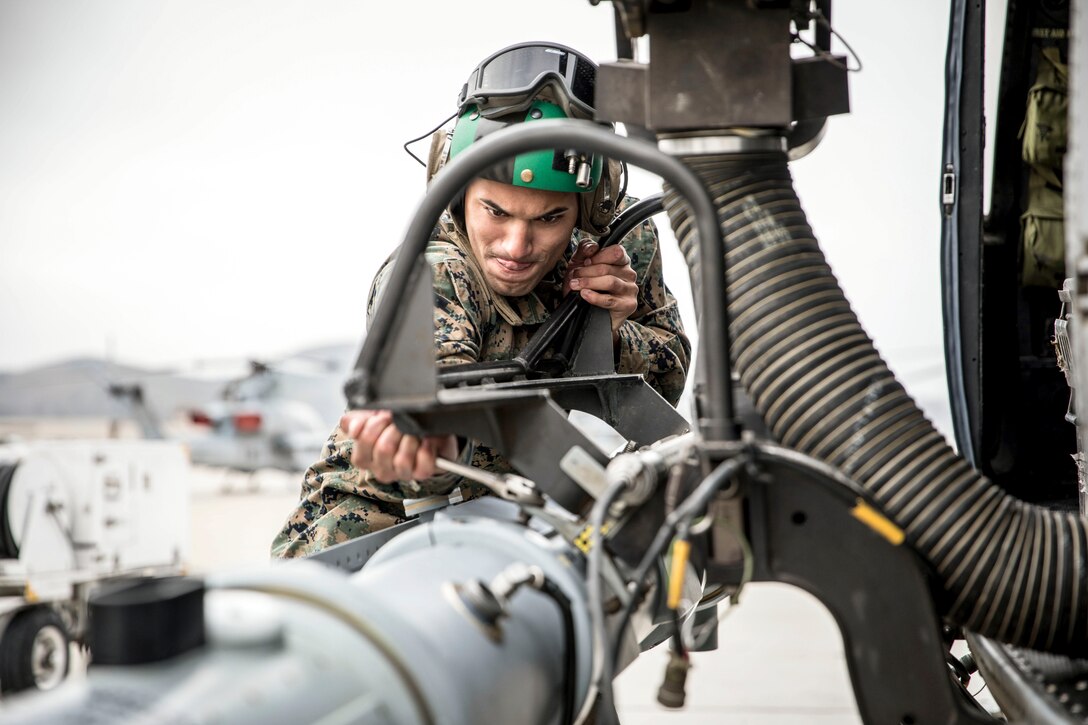A Marine Corps pilot uses a wrench on a weapon system being connected to an aircraft.