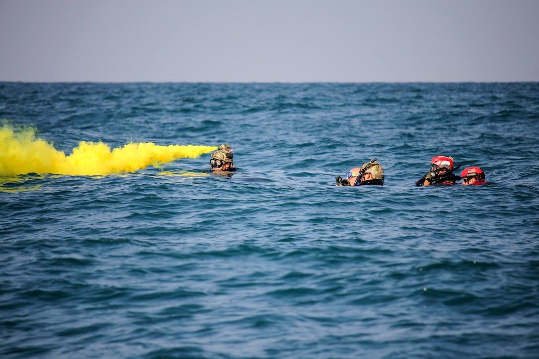 An airman releases a yellow smoke from a canister while floating next to fellow airmen in a body of water.