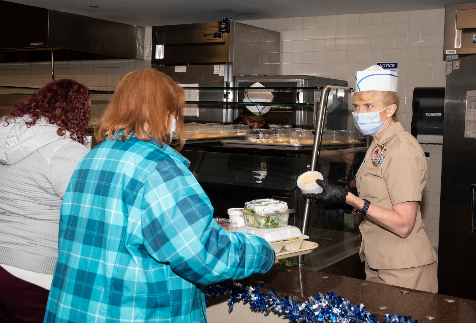 Naval Medical Center Portsmouth’s (NMCP) leadership and members of the Command Executive Board devoted time to NMCP’s galley serving lines for a holiday meal, Dec. 8. Capt. Shelley Perkins, NMCP's commanding officer, serves dessert as part of the NMCP holiday meal served to nearly 240 staff and patients. The menu included shrimp cocktail, New England clam chowder, roast turkey, ribeye, and ham, among other holiday classics like mashed potatoes, asparagus, glazed carrots and macaroni & cheese, with a dessert selection of assorted pies and cookies.