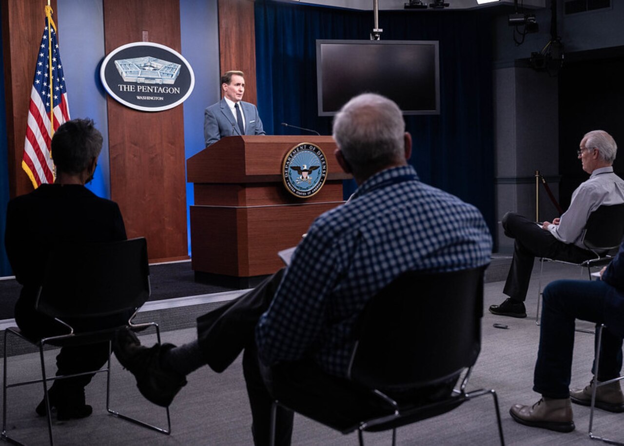 A Man stands at a lectern, speaking into a microphone. The sign behind him indicates that he is at the Pentagon.