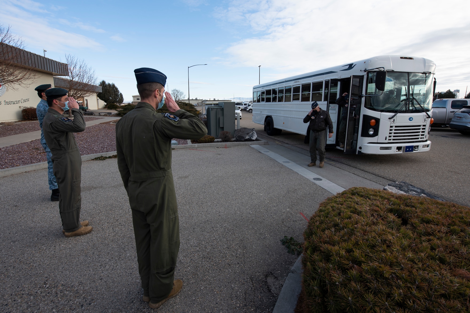 Two U.S. Air Force Airmen and one Republic of Singapore Air Force Airman solute a bus as it arrives to their squadron