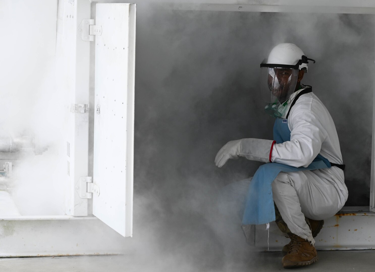 An Airmen in protective equipment stands in mist during a LOX quality control test