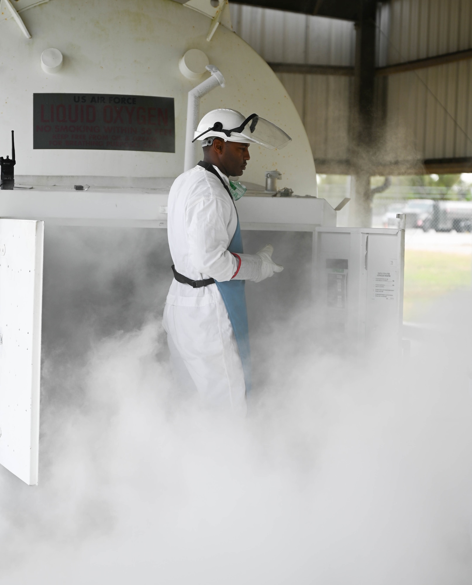 An Airmen in protective equipment stands in mist during a LOX quality control test
