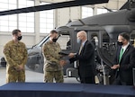 Two U.S. Air Force officers in uniform accept a log book and shake hands with two men in business suits in front of a helicopter.