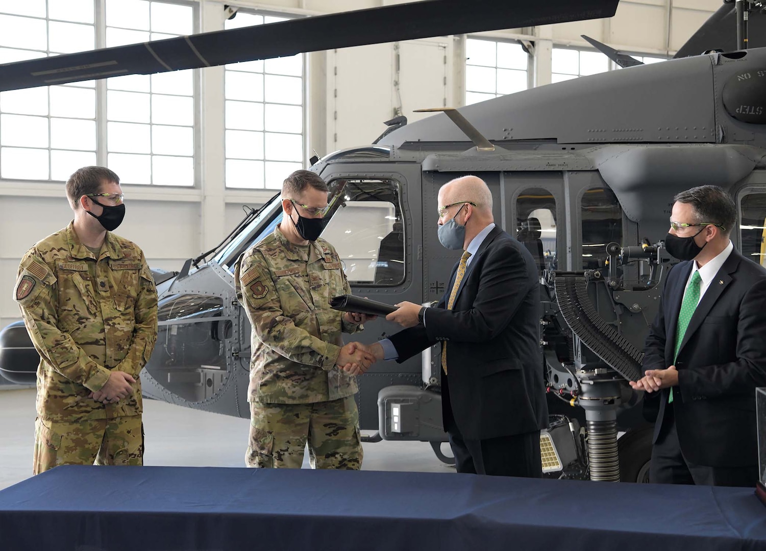 Two U.S. Air Force officers in uniform accept a log book and shake hands with two men in business suits in front of a helicopter.