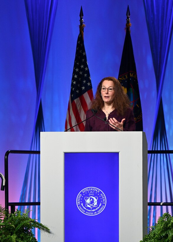 Image of person on stage behind a podium, presenting to an audience.