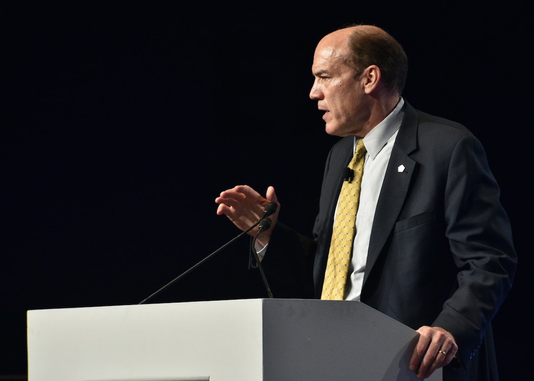 Image of person on stage behind a podium, presenting to an audience.