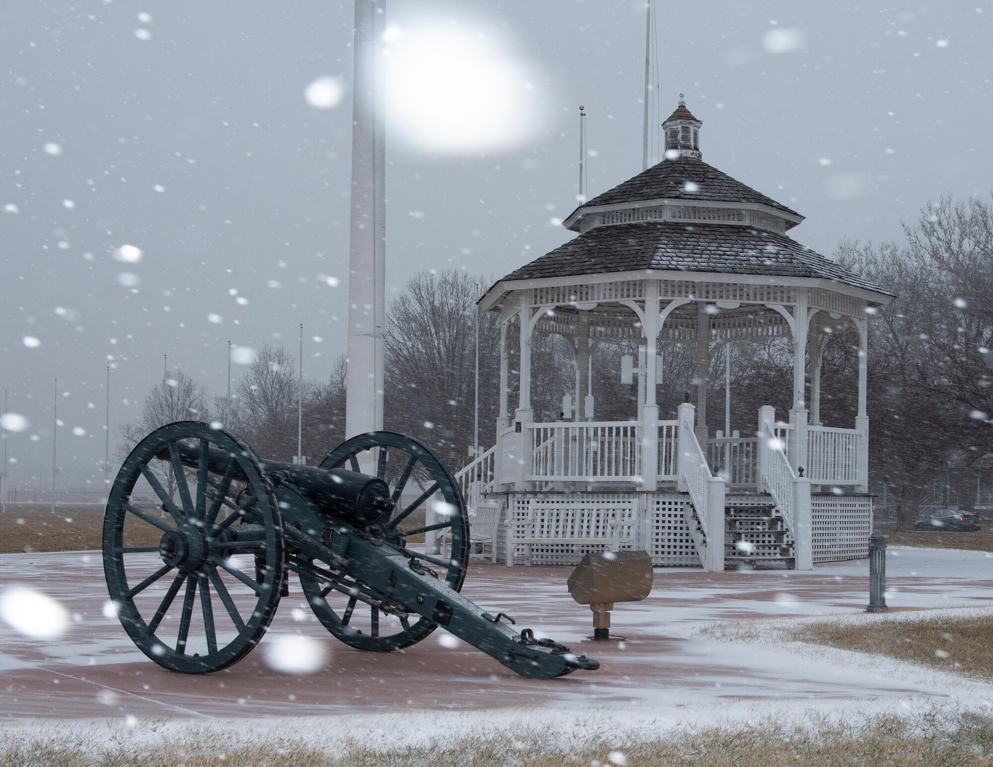 Snow falling on the gazebo and cannon on the parade grounds.