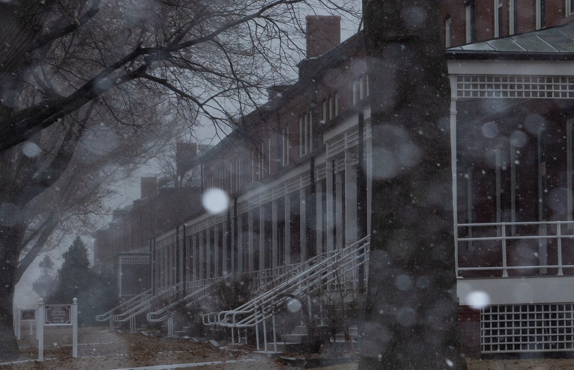Snow falling in front of brick buildings on base