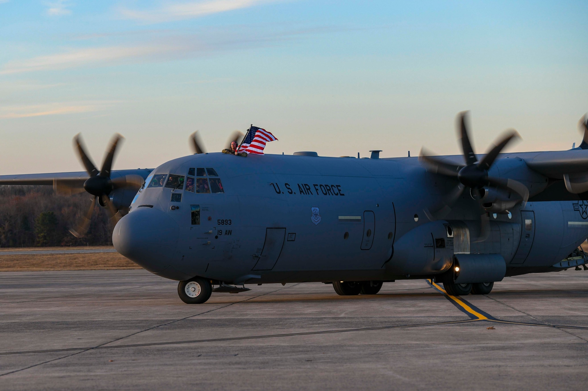 An Airman waves a flag on top of a C-130.