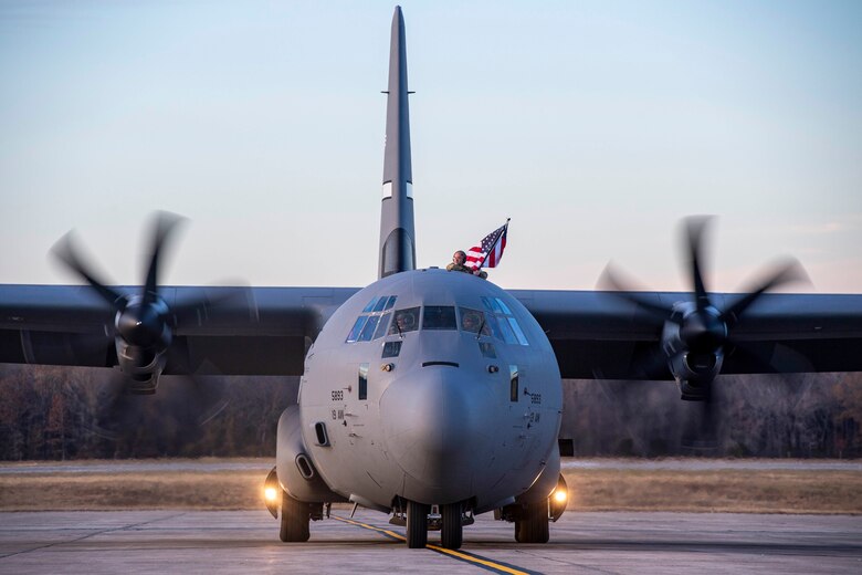An Airmen waves a flag on top of a C-130.