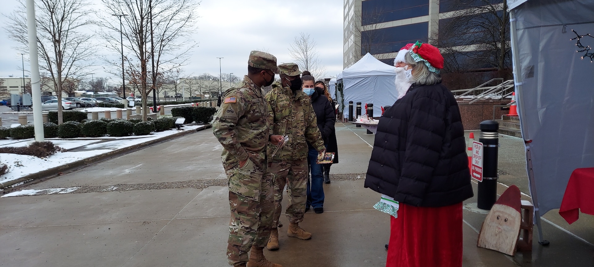 DLA Land and Maritime Acquisition Executive Mark Brown, and his wife Gail, dressed as Santa and Mrs. Claus greet two men in military OCP uniforms.