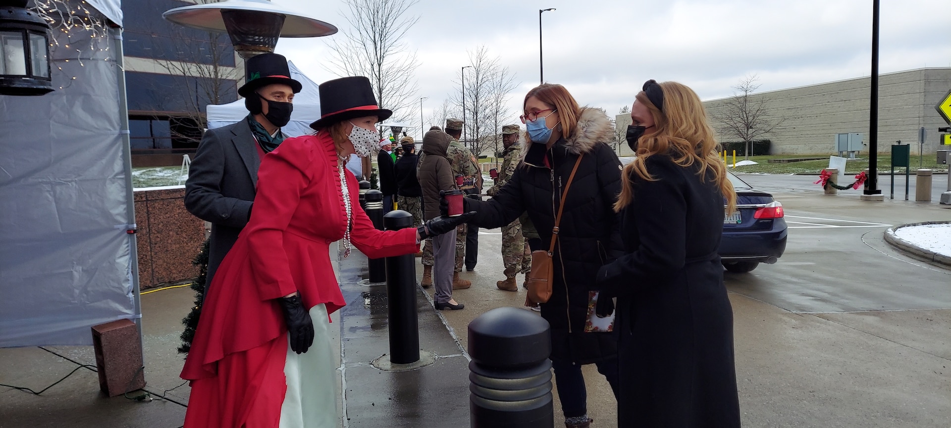 DLA Land and Maritime Deputy Commander Kenneth Watson, his wife Jill greet associates. They are dressed in a Christmas Carol attire. They are greeting two women in winter coats.