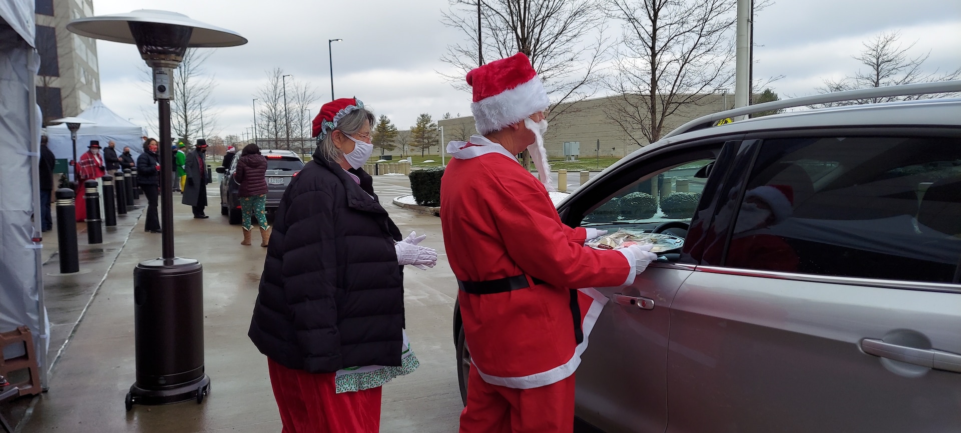 DLA Land and Maritime Acquisition Executive Mark Brown, and his wife Gail, dressed as Santa and Mrs. Claus hand out cookies to people in a car.